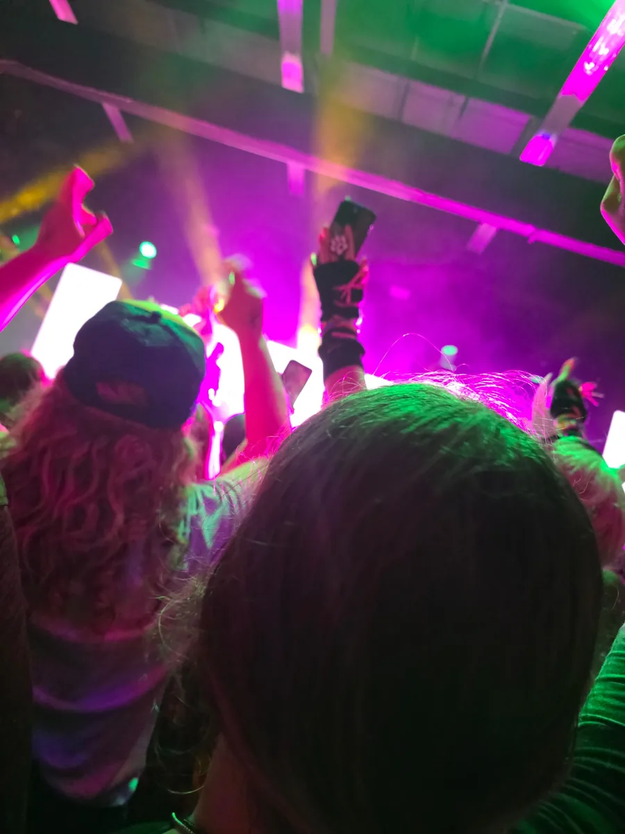 Concert crowd holding phones up under pink and green stage lights