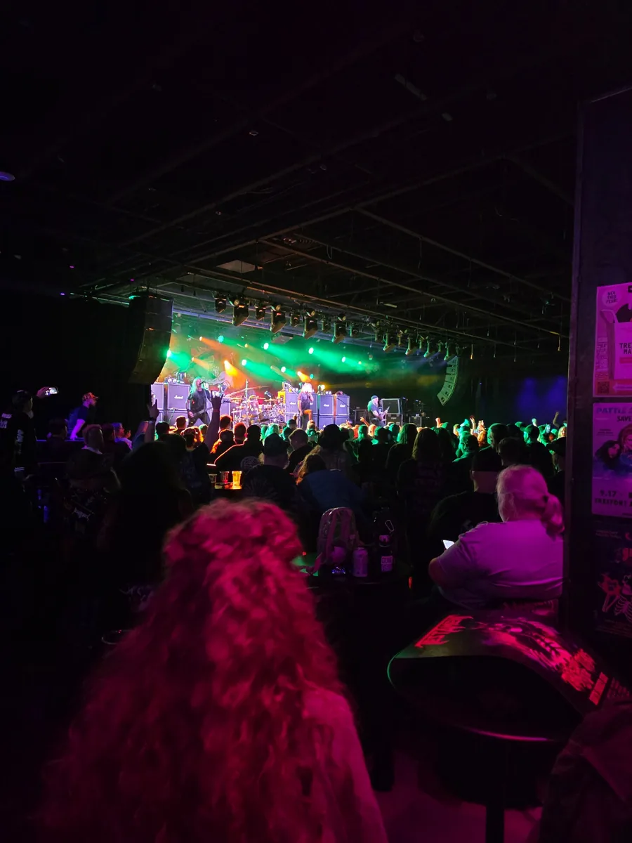 Wide crowd view at a live Testament show with green stage lights
